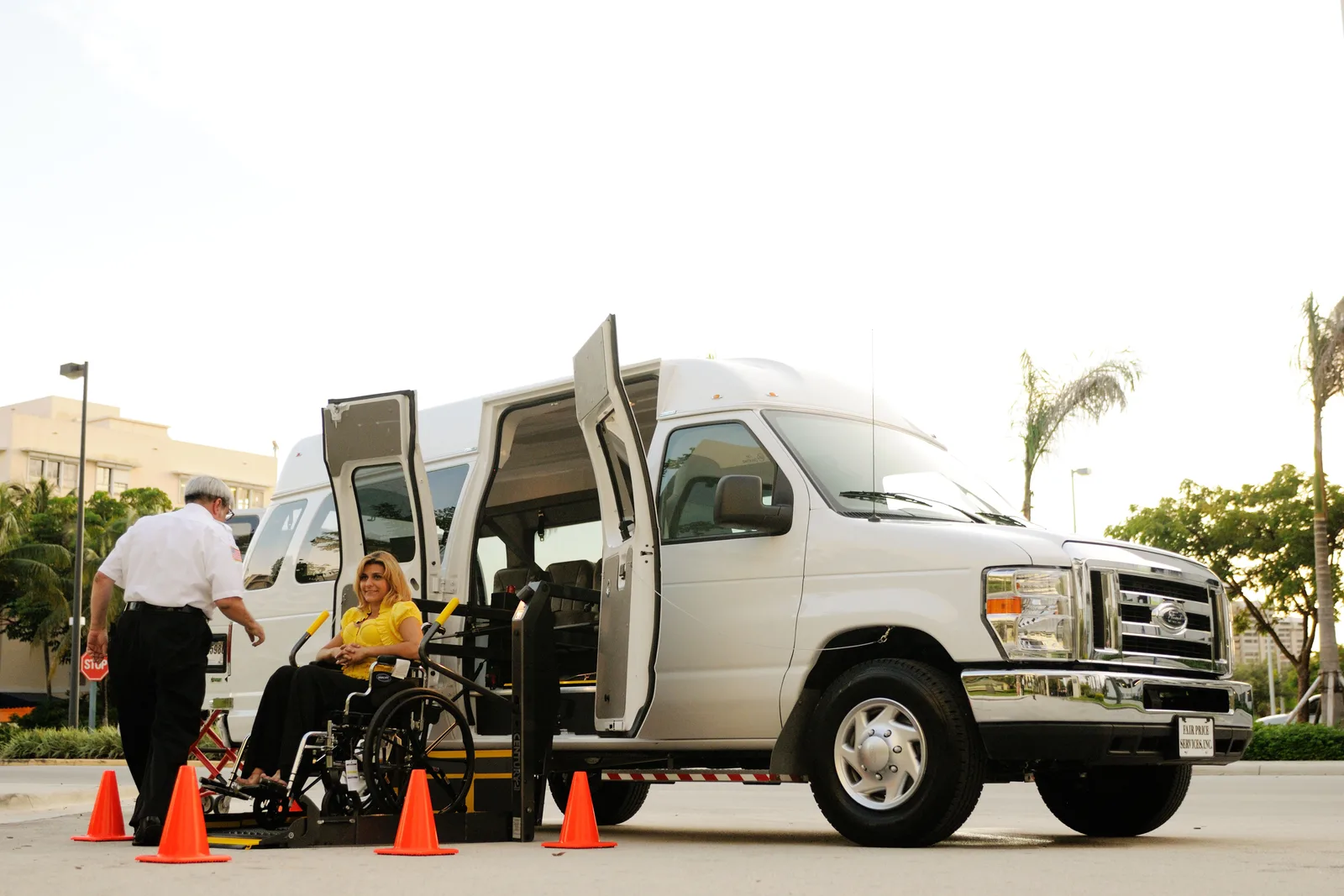 A person in a wheelchair uses a lift to board a van, assisted by a driver. Outdoor setting with cones. 4 checks for accessible USA travel in trail towns