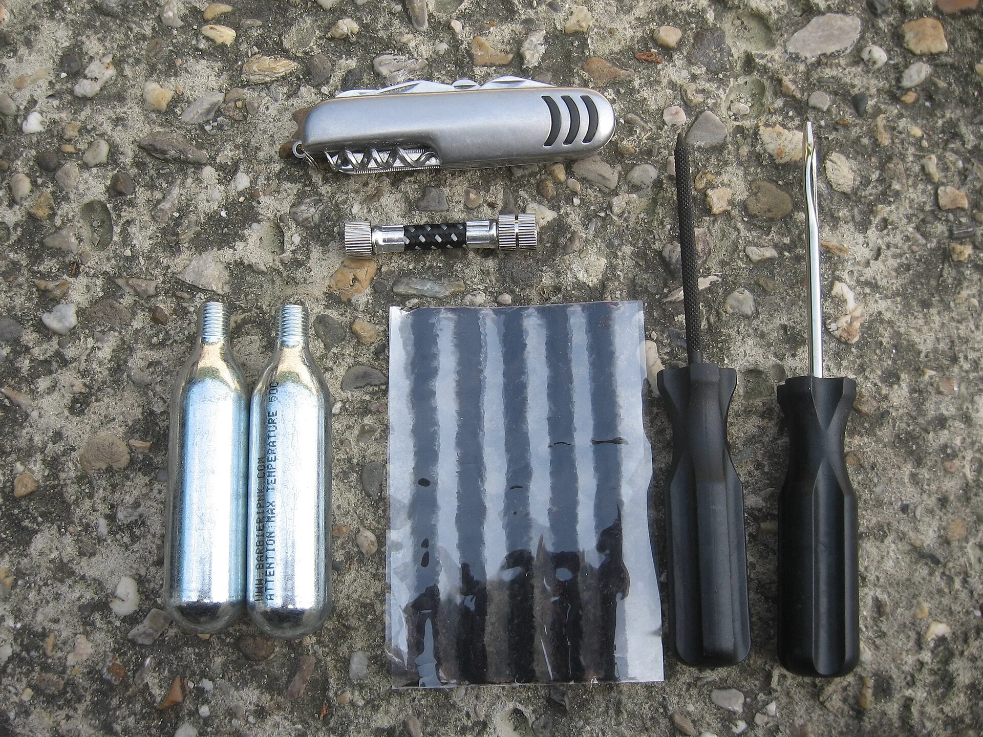 Tubeless repair kit with CO2 cartridges and a connector, a file, "salamis" and an eye tool. Pocket knife above. What to Pack for a Trail Town Ride: Repairs, Visibility, Weather and Town Clothes