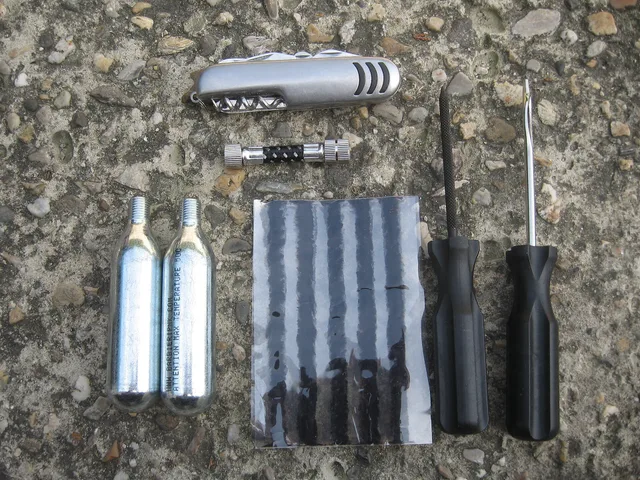 Tubeless repair kit with CO2 cartridges and a connector, a file, "salamis" and an eye tool. Pocket knife above. What to Pack for a Trail Town Ride: Repairs, Visibility, Weather and Town Clothes